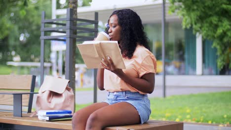 Chica-Estudiante-Leyendo-Un-Libro-Y-Tomando-Café.-Concepto-De-Educación,-Escuela-Y-Personas.-Chica-Estudiante-Afroamericana-Feliz-Y-Sonriente-Leyendo-Un-Libro-Y-Tomando-Café-Para-Llevar-En-La-Ciudad.